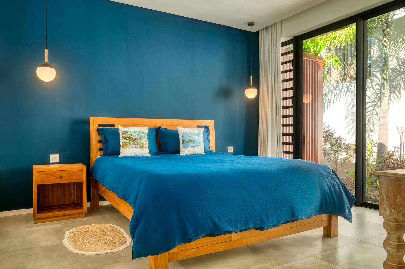 Chambre à coucher bleue spacieuse avec mur bleu, lit double en bois et large baie vitrée dans une villa 3 chambres à l'Île Maurice.