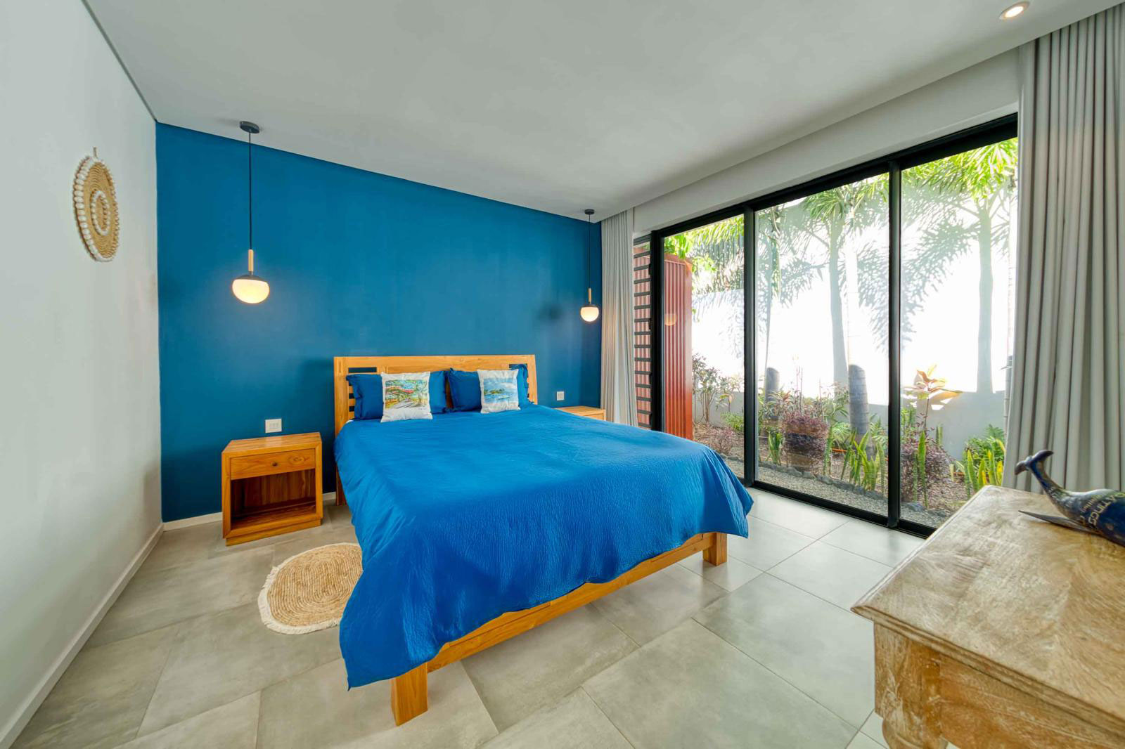 Chambre à coucher spacieuse avec mur bleu, lit double en bois et large baie vitrée dans une villa 3 chambres à l'Île Maurice.